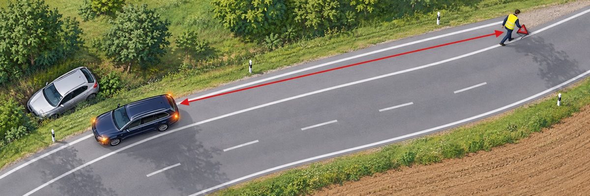 Unfallstelle absichern, Draufsicht auf eine Landstraße: Unfallauto im Graben, dahinter das Helferauto mit Warnblinker, Person in Warnweste geht am Fahrbahnrand dem Verkehr entgegen und stellt das Pannendreieck vor einer Kurve auf – rote Abstandspfeile.